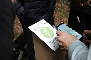 Eine Besucherin scannt den QR-Code der Hörstation „Morgendliches Waldkonzert“
